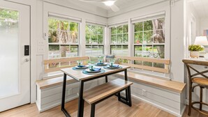Une cuisine avec un banc en bois, une table sur laquelle sont disposés des verres, et de grandes fenêtres donnant sur un paysage verdoyant.