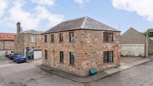 A stone building with a sloped roof, multiple windows, and a small porch area. - The Howff - Lovely 2-bed Apartment in Anstruther (Anstruther)