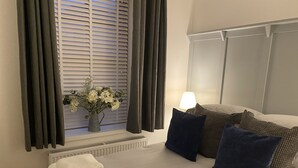 A neatly made bed with a patterned bedspread, a stack of folded towels, and a vase with flowers on a windowsill. - The Howff - Lovely 2-bed Apartment in Anstruther (Anstruther)