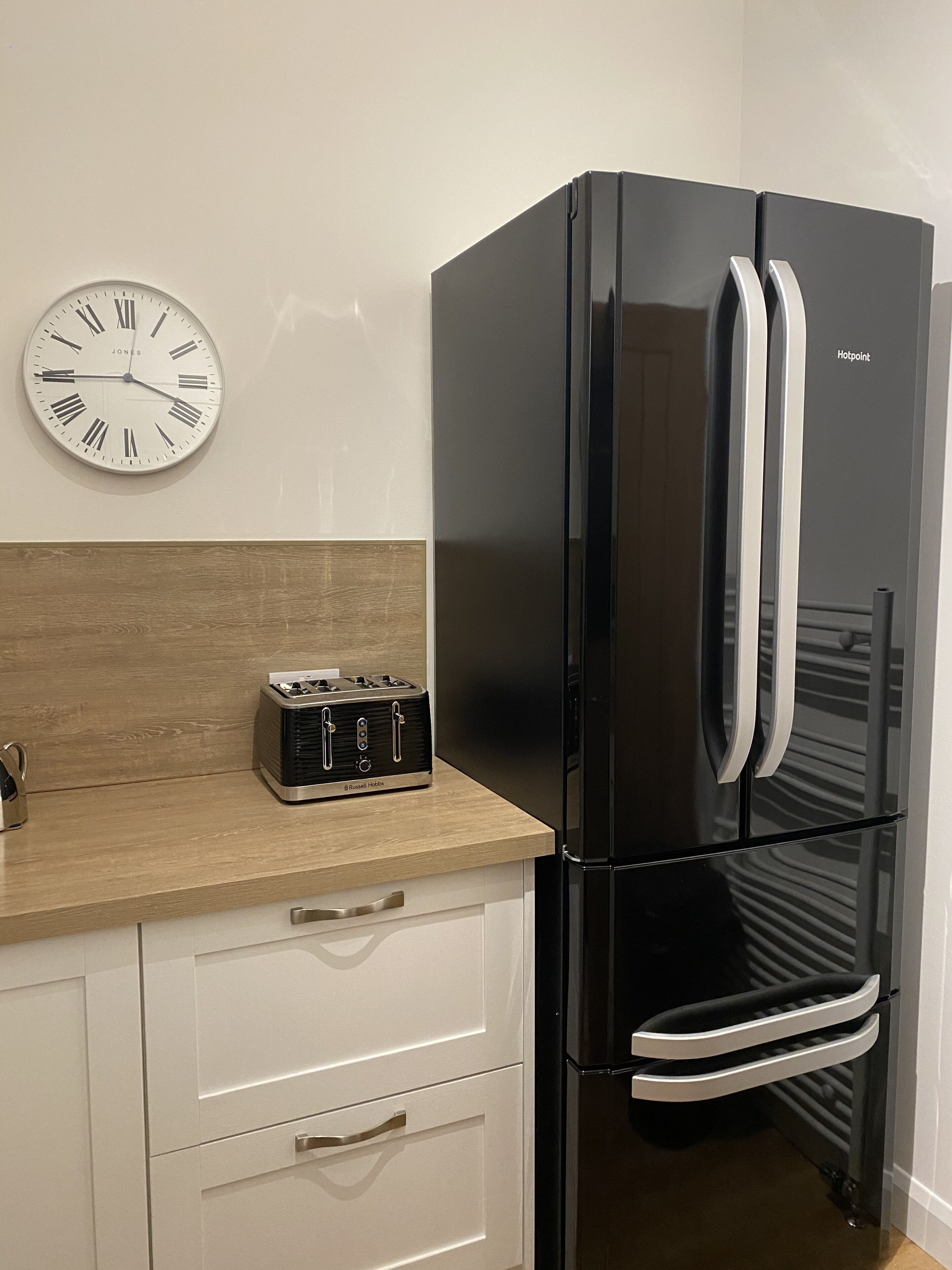 Uma cozinha com geladeira preta, bancada de madeira, relógio na parede e torradeira.