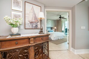 Um quarto com uma cama, um penteou, um vaso com flores e uma pintura de um veleiro na parede.