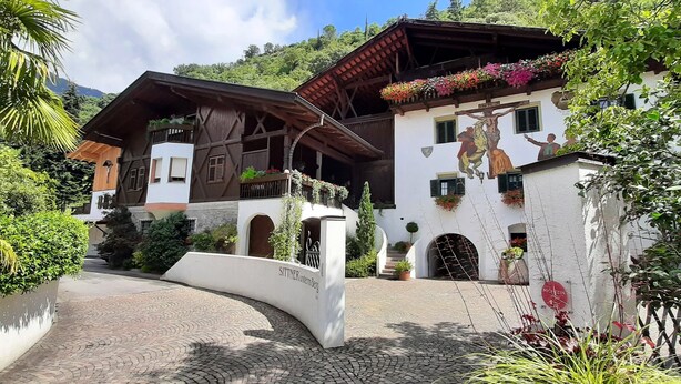 A traditional chalet with a wooden facade, balconies with flower boxes, and a mural of Jesus Christ on the wall. - Agriturismo Sittnerhof - a place to stay for those seeking relaxation in Meran e (Meran)