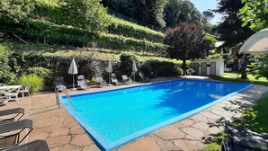 A rectangular swimming pool with lounge chairs and umbrellas, surrounded by lush greenery and stone pathways. - Agriturismo Sittnerhof - a place to stay for those seeking relaxation in Meran e (Meran)
