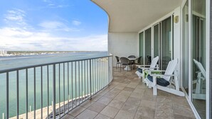 A balcony with a view of the sea, white chairs, and a table.