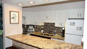 Cozinha com armários brancos, bancadas de granito e painel de azulejos preto e branco.