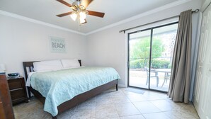 Quarto com cama, mesa de cabeceira, ventilador de teto, porta de vidro deslizante e um aviso na parede.