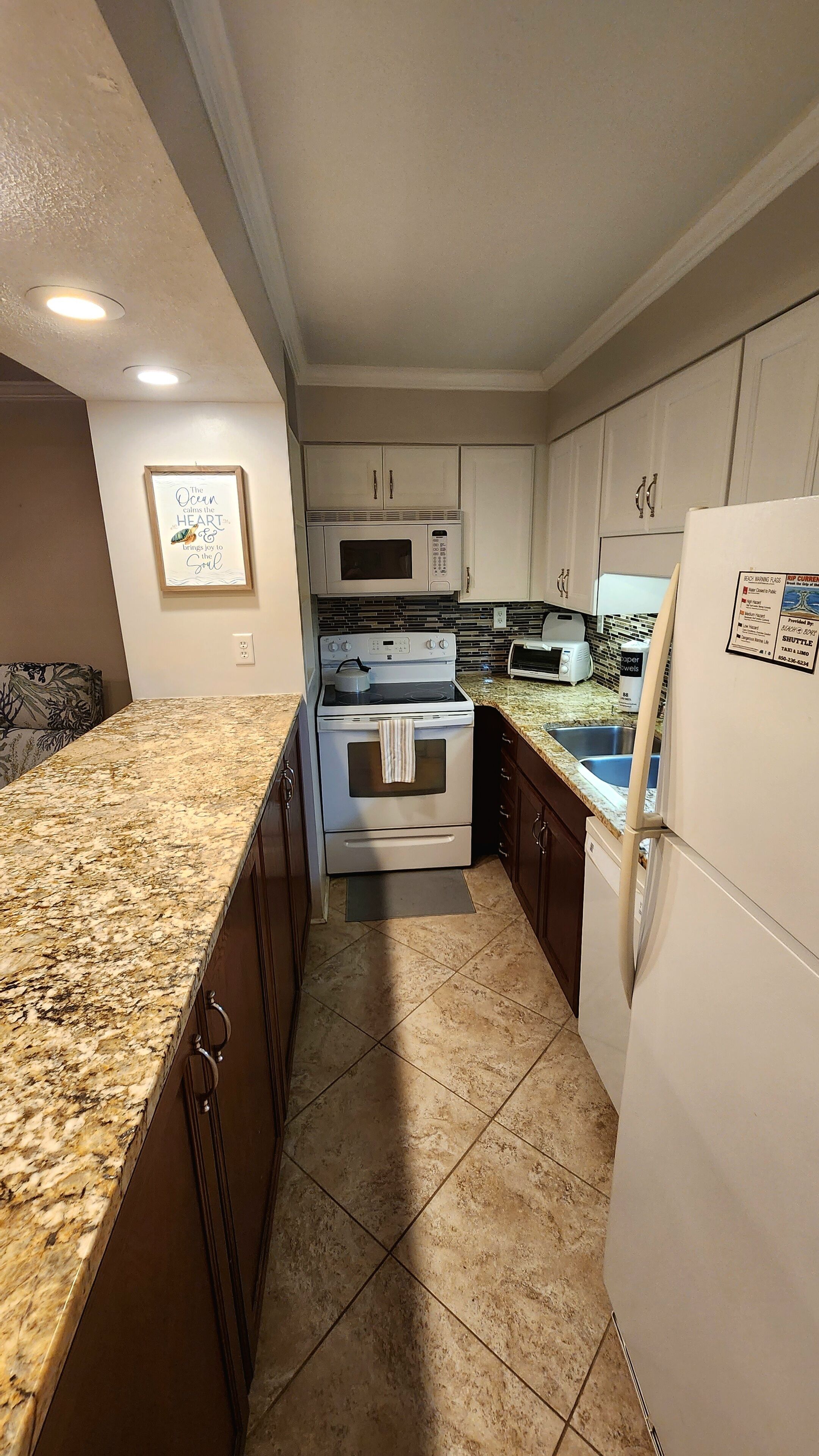 A compact kitchen with a granite countertop, stainless steel appliances, and a tiled backsplash.