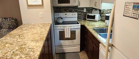 A compact kitchen with a granite countertop, stainless steel appliances, and a tiled backsplash.