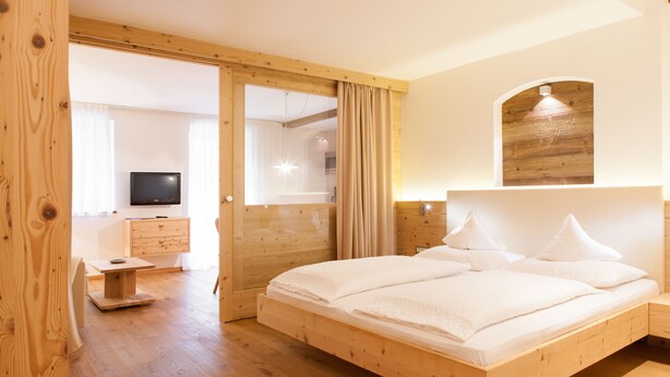 A wooden-framed bedroom with a bed, a desk, and a television in the background. - Unwind - relax - seek peace - enjoy - Merano is my holiday destination (Meran)