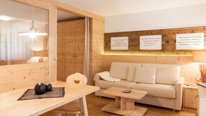 A modern, minimalist living room with a wooden floor, a beige sofa, a wooden dining table with two vases, and a hanging light fixture. - Unwind - relax - seek peace - enjoy - Merano is my holiday destination (Meran)