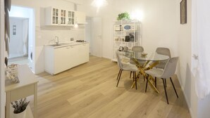 A modern kitchen with white cabinets, a glass dining table with chairs, and a white shelving unit with various items. - 2 Rooms at the Colosseum Rome New Apartment (Roma)