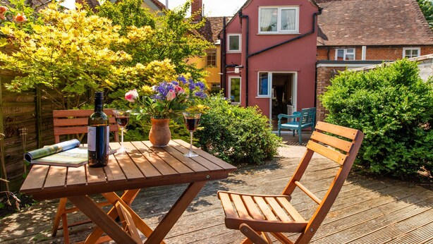Een houten tafel met een fles en glazen, een stoel en een boek op een terras.