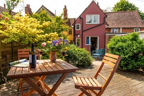 Een houten tafel met een fles en glazen, een stoel en een boek op een terras.