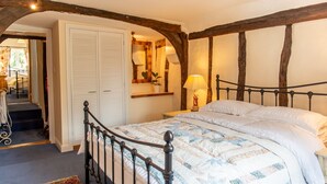 Een slaapkamer met een hemelbed, houten plafond, een witte kledingkast en een klein tafeltje met een lamp.
