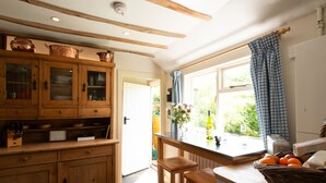 A kitchen with wooden cabinets, a window with curtains, and a table with fruit. - A romantic little Flax Workers Cottage with a beautiful open fire and an enclosed garden which leads (Long melford)