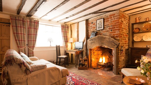 A cozy living room with a fireplace, a sofa, and a table with a laptop. - A romantic little Flax Workers Cottage with a beautiful open fire and an enclosed garden which leads (Long melford)