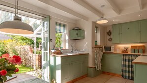 A kitchen with green cabinets, a wooden countertop, and a window overlooking a garden. - A beautiful little Victorian House in one of Suffolk’s prettiest villages. (Cavendish)
