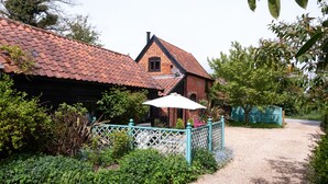 Une maison traditionnelle en briques, avec un toit recouvert de tuiles rouges, une clôture blanche et une allée gravillonnée.