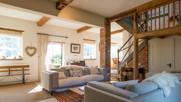 A spacious living room with a large sofa, a smaller armchair, and a coffee table. There is a staircase with a wooden railing leading to an upper level. - Five Star style with beautiful views of idyllic Countryside: The Old Steam Mill (Hartest)