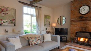 A living room with a grey sofa, a wooden coffee table, a fireplace, a television, and artwork on the walls. - Five Star style with beautiful views of idyllic Countryside: The Old Steam Mill (Hartest)