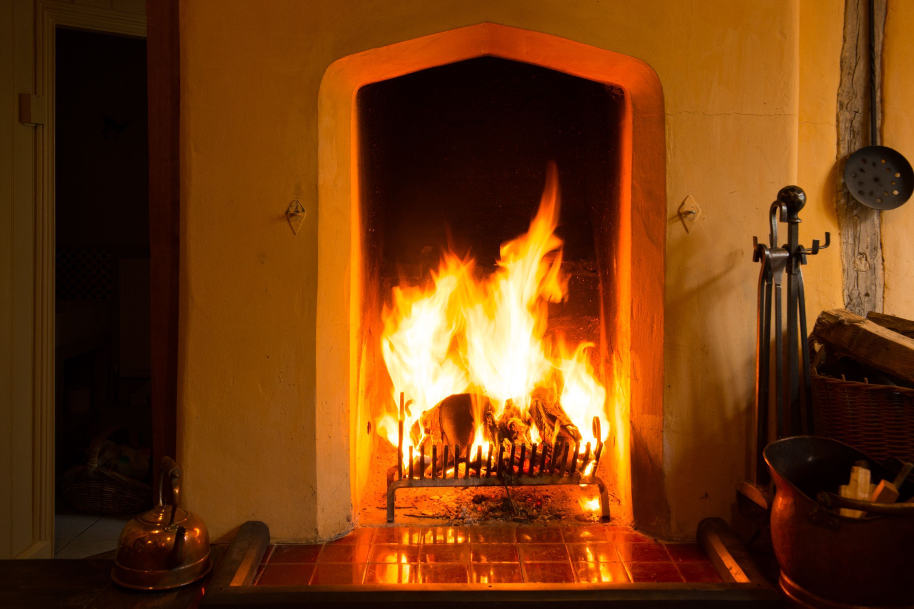 A fireplace with a metal screen, a kettle, and a bucket of wood.