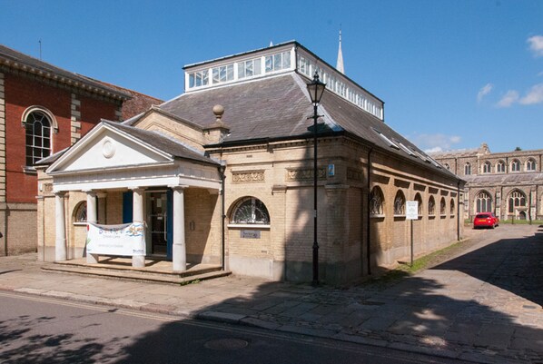 A historic building with a prominent entrance, a clock tower, and a red car parked nearby.