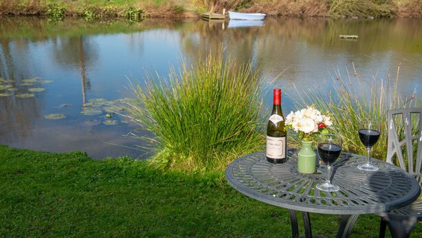 Ein Tisch mit einer Weinflasche, einem Blumenstrauß und zwei Weingläsern an einem Teich.