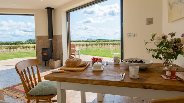 Ein Essbereich mit großem Fenster, Kamin und Tisch, gedeckt mit Brot, Obstschale und Blumen.