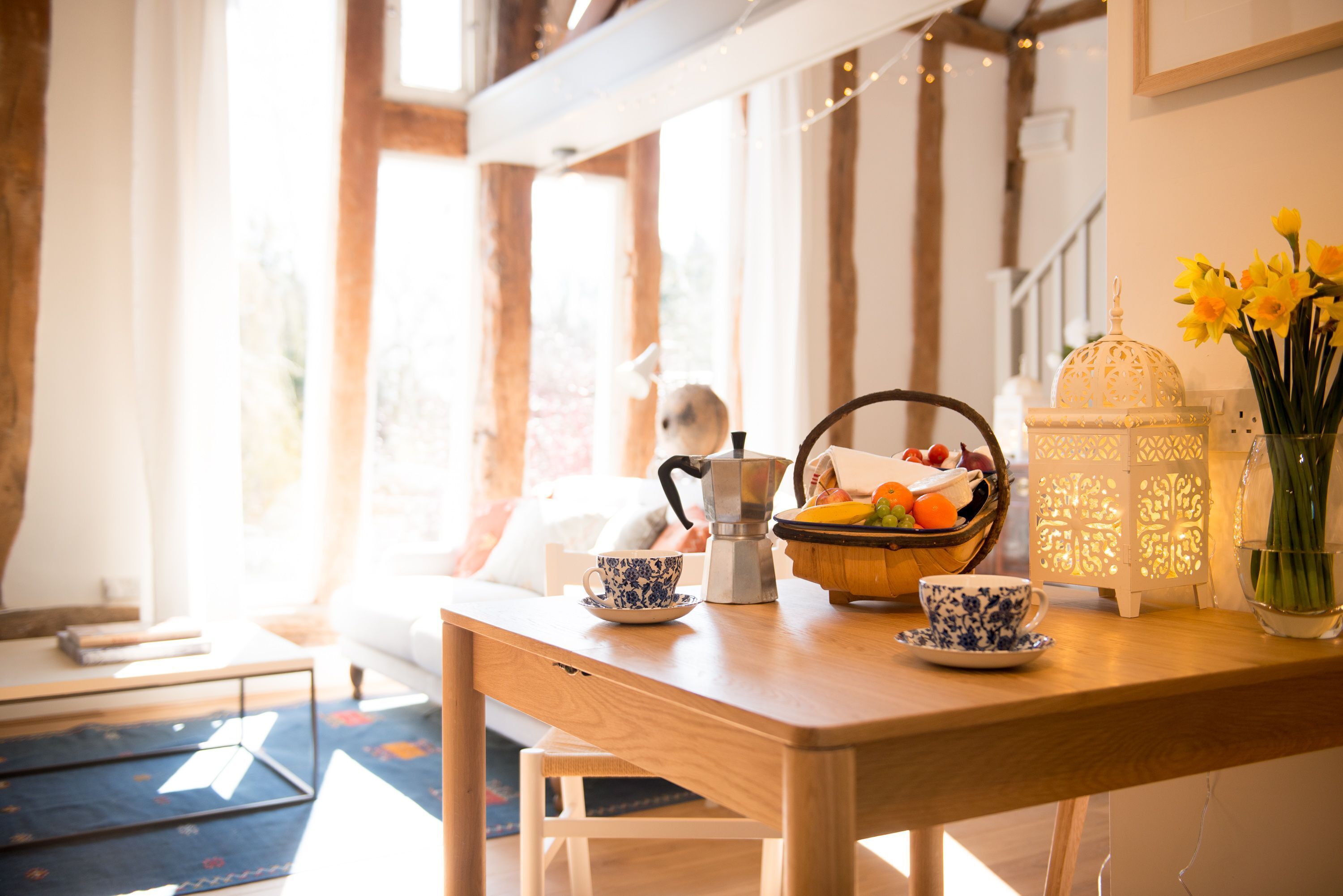 Une table en bois avec une machine à café, un panier de fruits et un vase de fleurs.