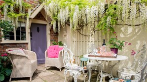 A cozy outdoor seating area with wicker furniture, a table with drinks, and hanging white flowers.