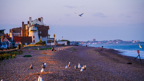A pebbled beach with a building and a view of the sea.