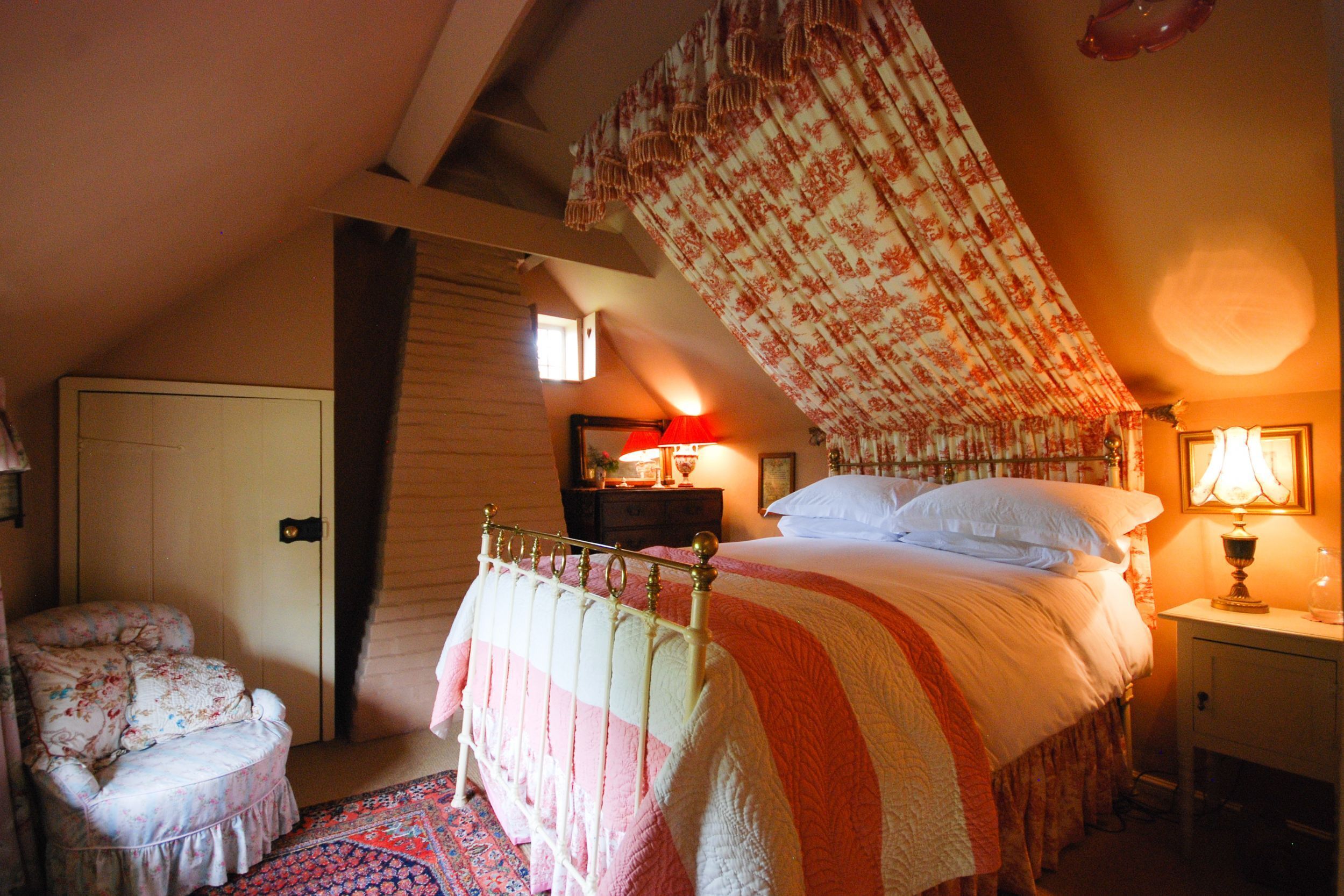 Un dormitorio con cama, una silla, una mesita de noche y una lámpara.