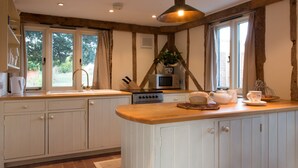 Una cocina con armarios blancos, encimera de madera, horno empotrado, microondas y una ventana con cortinas.