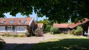 Une maison de campagne avec une allée en gravier, une clôture en bois et un jardin agrémenté de plantes à fleurs.