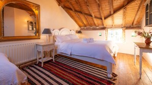 Une chambre avec un plafond en bois, un grand miroir, un lit avec du linge de lit blanc, une table de chevet avec une lampe et un tapis à rayures.