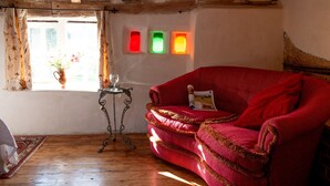 Une pièce chaleureuse avec un canapé rouge, une petite table ornée d’un vase et d’une bouteille, et une fenêtre avec des rideaux.