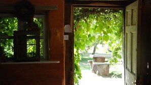 Une porte ouverte donnant sur un jardin où se trouvent un banc et un arbre.