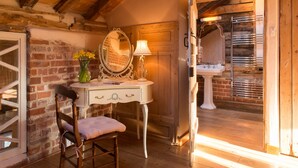 A rustic room with a wooden ceiling, a white vanity with a mirror, a chair, and a brick wall. - Dons Barn - A romantic holiday cottage with beautiful, beamed interiors. Wow. (Edwardstone)
