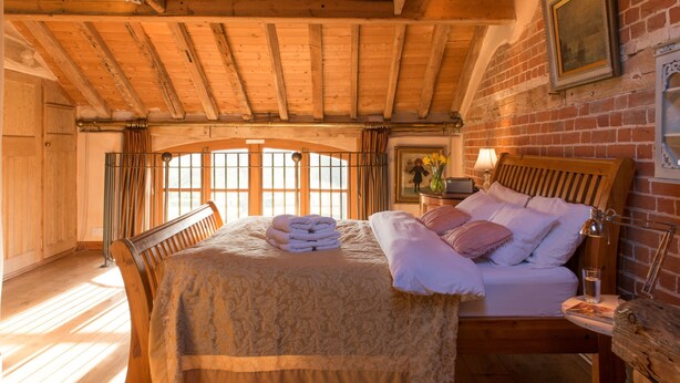 A cozy bedroom with a wooden bed, a nightstand, and a window with curtains. - Dons Barn - A romantic holiday cottage with beautiful, beamed interiors. Wow. (Edwardstone)