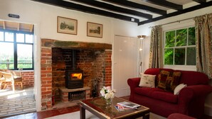 A cozy living room with a brick fireplace, a red sofa, and a coffee table. - Remote, Comfort, Sea Views, and the romance of the beautiful Essex Marshes - The Wobbin (Tollesbury)