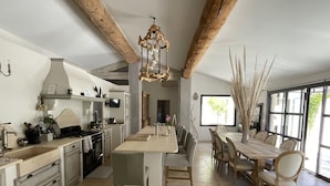 A spacious kitchen with a central island, wooden beams, a chandelier, and a dining area with a large window. - Beautiful contemporary villa, swimming pool and large garden (Berre-l'Étang)