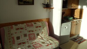 A cozy room with a wooden headboard sofa, a kitchen with wooden cabinets, and a painting on the wall. - Studio cabin for 4 near slopes, Southwest exposure in Chamrousse (Chamrousse)