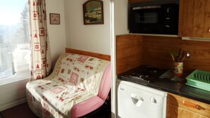 A compact kitchen with a microwave, a stove, and a sink. There is a bed with a patterned blanket and a window with curtains. - Studio cabin for 4 near slopes, Southwest exposure in Chamrousse (Chamrousse)