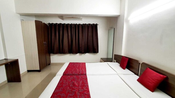 A hotel room with a large bed, a wardrobe, a mirror, and a window with curtains. - Hotel Bhooshan Airport Road (Pune)