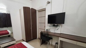 Ein Schlafzimmer mit einem Bett, einem Schreibtisch, einem Kleiderschrank, einem Fernseher und einem Mülleimer.