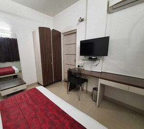 Une chambre à coucher comprenant un lit, un bureau, une armoire, une télévision et une poubelle.