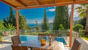 Un espacio exterior cubierto con piscina, mobiliario de madera y vistas a árboles y un paisaje distante.