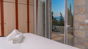 Un dormitorio con una cama, un par de toallas enrolladas y un ventanal corredero que da a un área exterior con piscina y árboles.