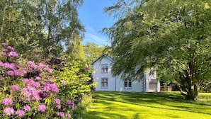 A white house with a well-maintained lawn and blooming pink flowers in the foreground.