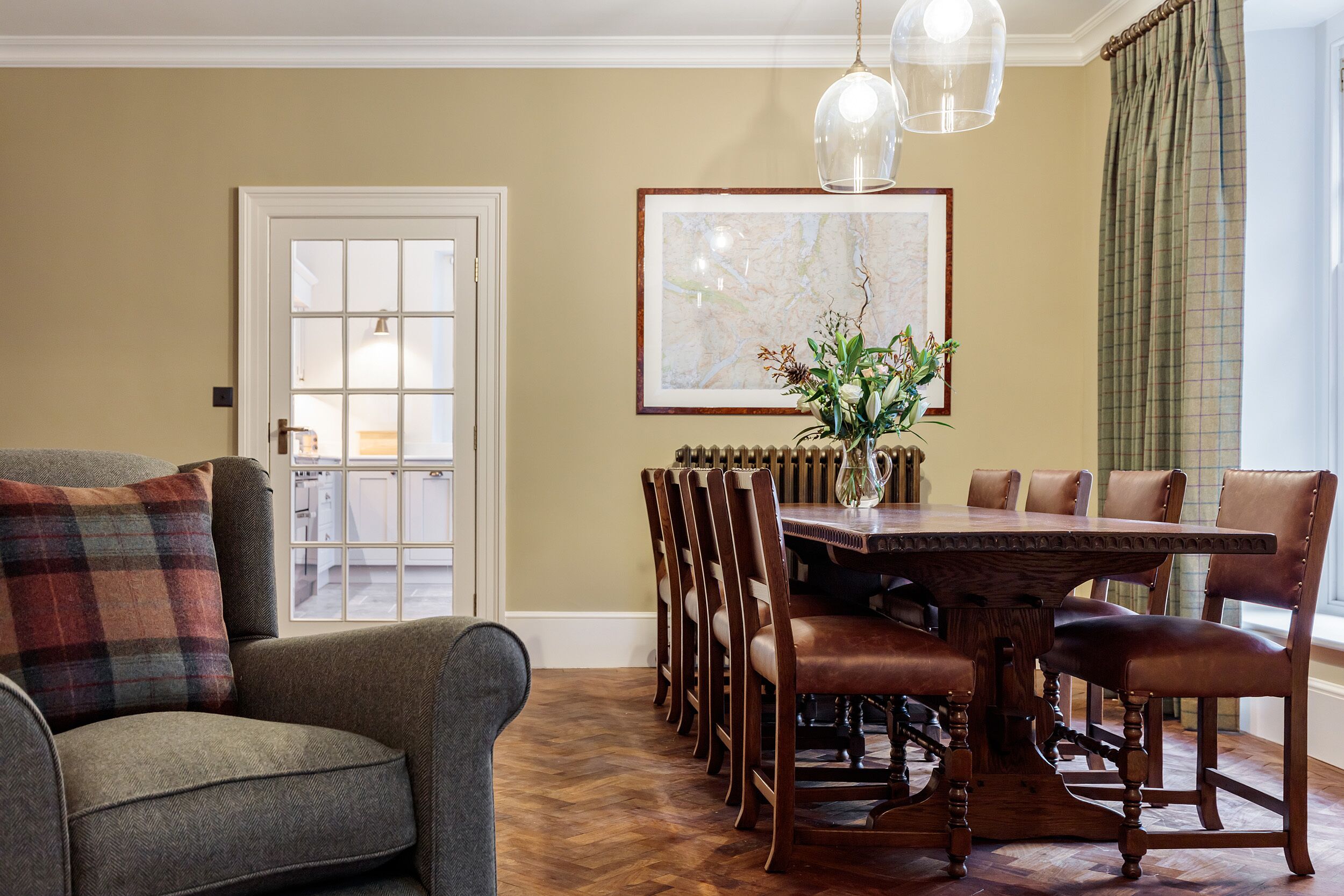 A dining area with a wooden table and chairs, a vase with flowers, and a map on the wall.